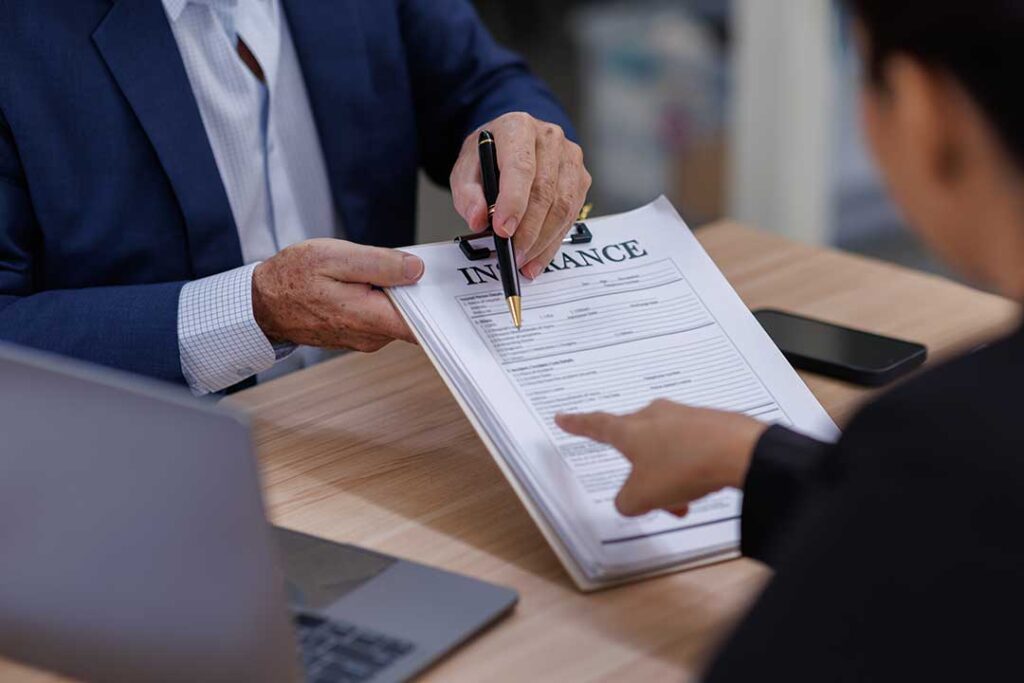 A couple reviews life insurance paperwork and beneficiary forms at a table with organized documents and a pen.