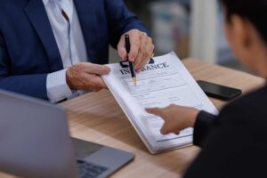 A couple reviews life insurance paperwork and beneficiary forms at a table with organized documents and a pen.